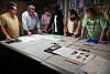 A professor and class review sketches and portfolio work in a shared conference room table.