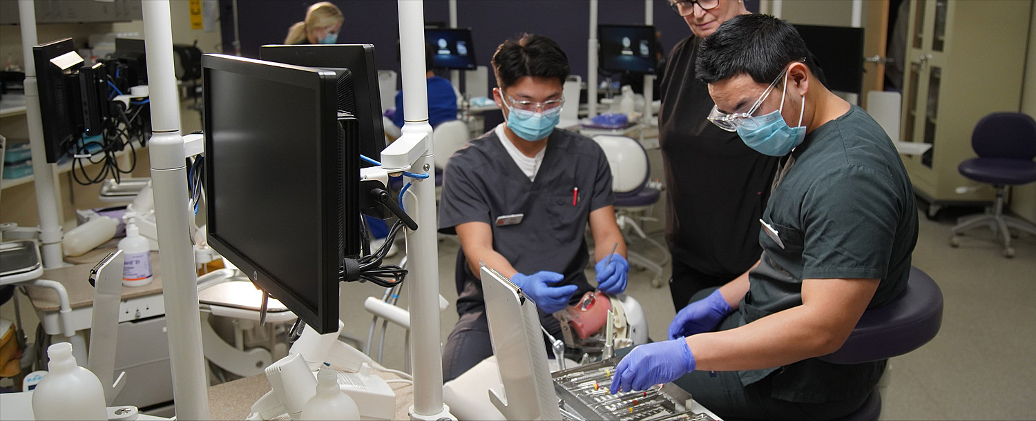 Two students practicing their skills on a test dummy in the dental clinic.