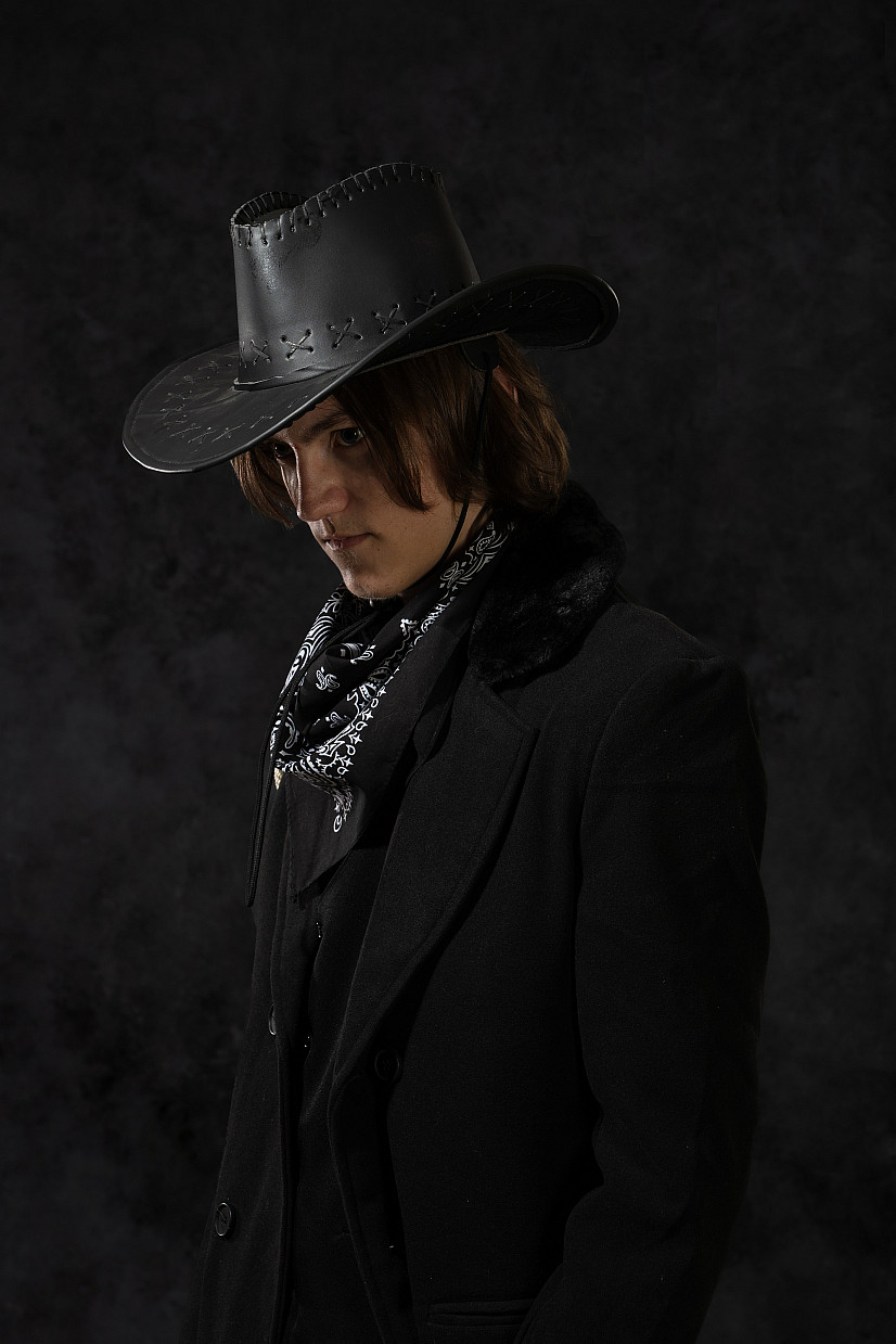Student photography work. The image captures a person looking down in a dark background with a black cowboy hat and handkerchief around t...