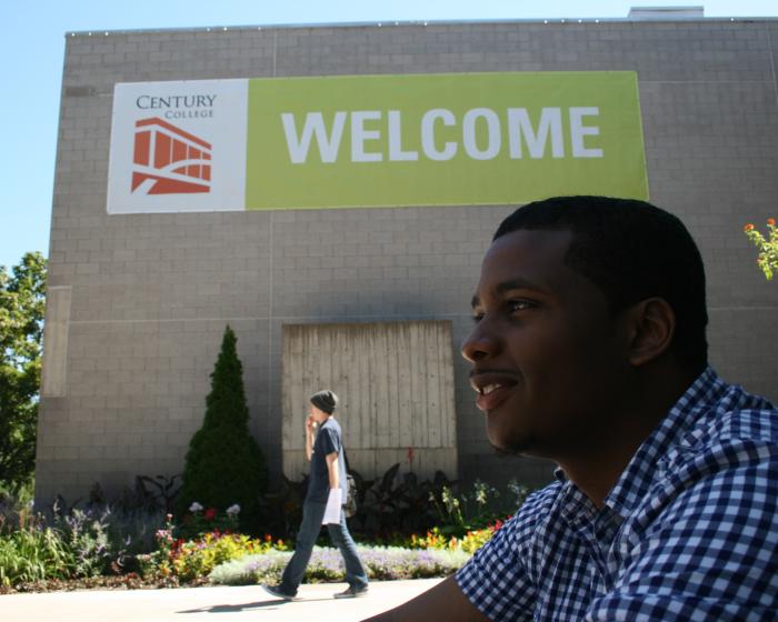 Student sitting outside with "Welcome" sign hanging up.