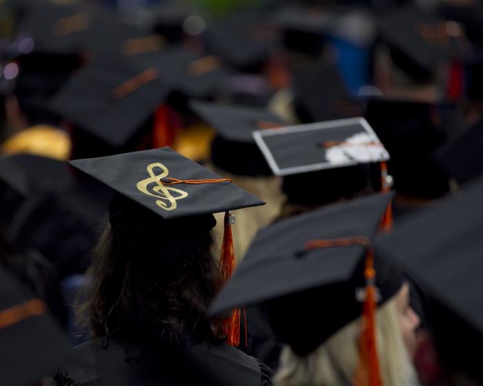 Image of graduates standing in crowd and a close up of a girl's graduation cap with a treble clef on it.